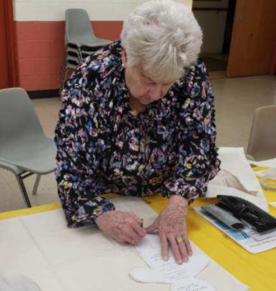 Woman leaning over a table writing on a piece of paper.