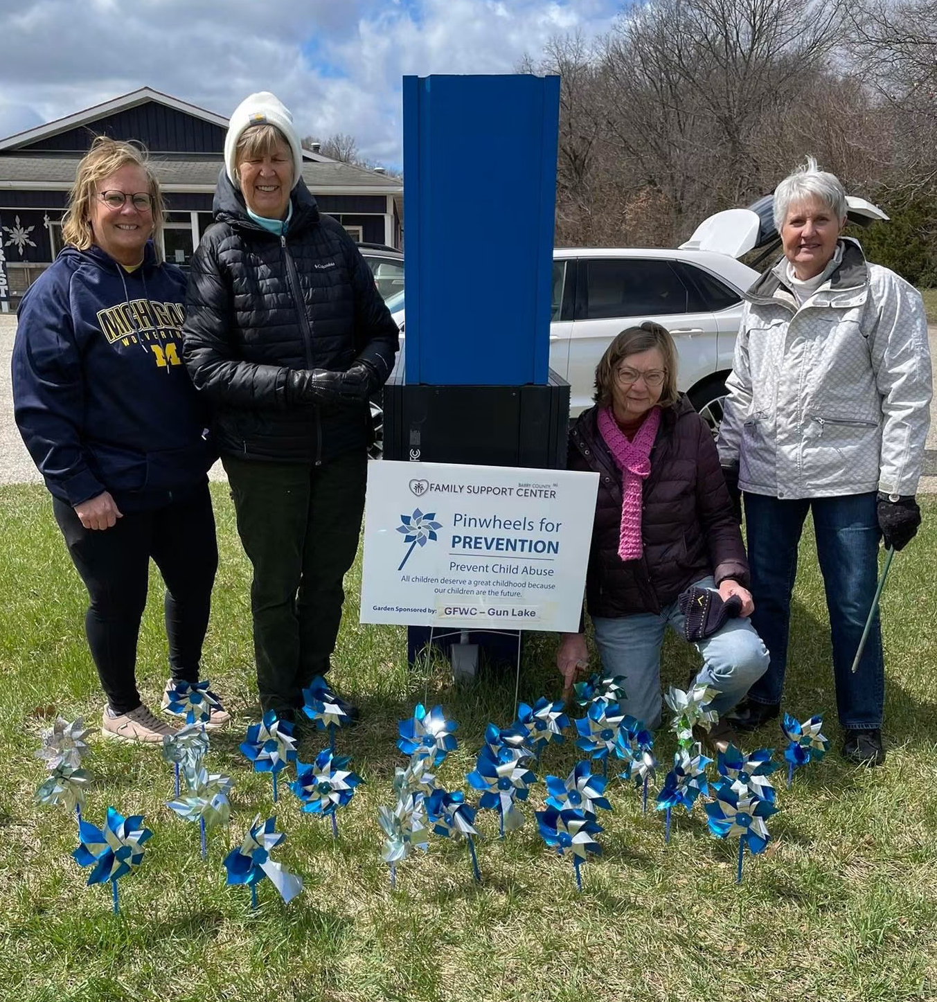 Four GFWC Gun Lake members standing behind their blue windmills supporting the Barry County Family Support Center